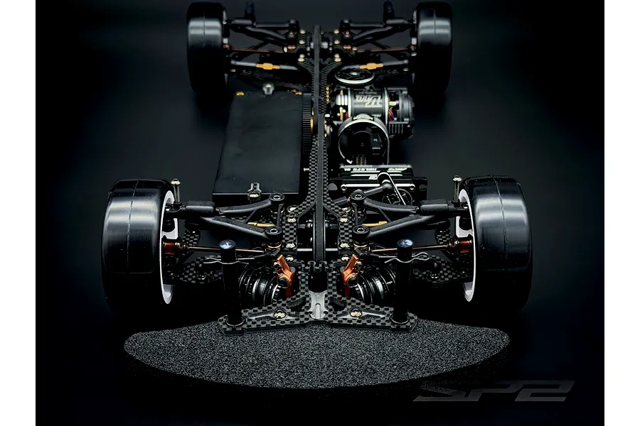 Top down front view of the RC Maker SP2 EP RC Touring Car chassis showing carbon fiber deck, suspension, and electronics on a dark background.