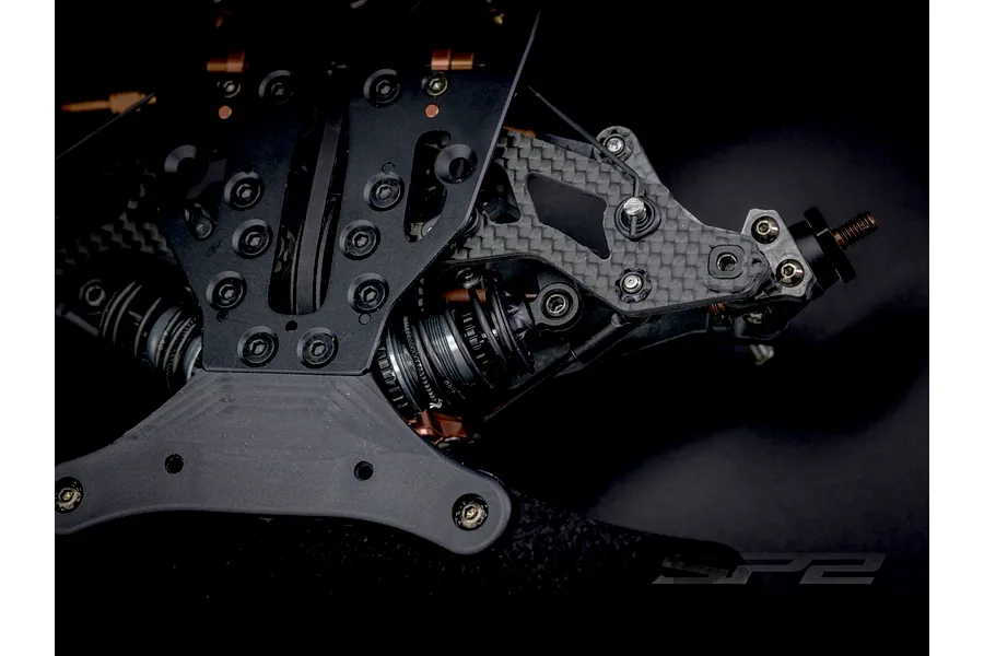 Close-up studio view of the carbon fiber suspension and chassis components of the RC Maker SP2 1/10 scale touring car kit.