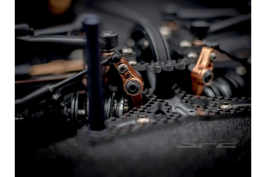 Close-up of RC Maker SP2 EP RC touring car chassis featuring carbon fiber parts and bronze metal linkage components.