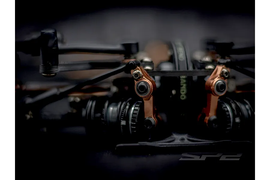 Close-up shot of the steering mechanism and bronze-coloured linkages on the RC Maker SP2 touring car kit chassis.