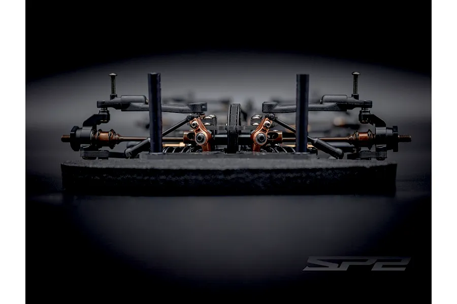 Close-up front-on view of the RC Maker SP2 EP RC touring car chassis highlighting suspension components and foam bumper.