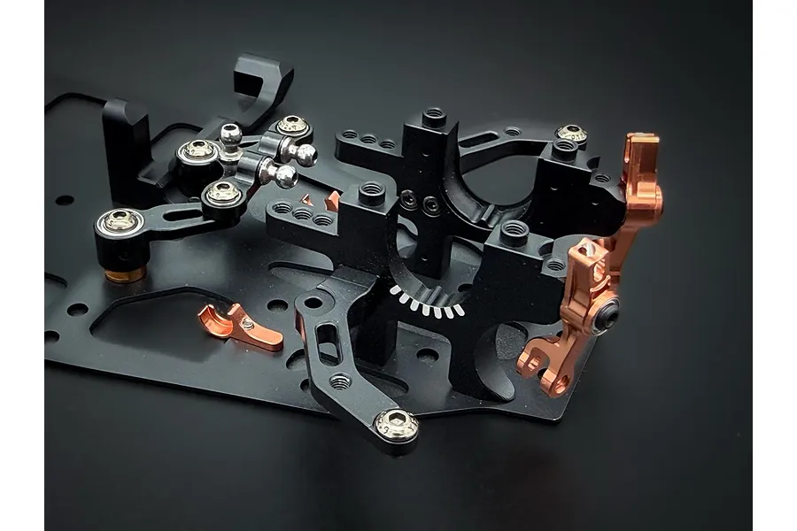 Close-up of black and copper anodised aluminium RC car chassis components and bulkheads on a dark background.