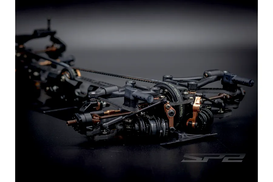Close-up angled view of the front suspension and chassis components of the RC Maker SP2 1/10 scale electric touring car kit.