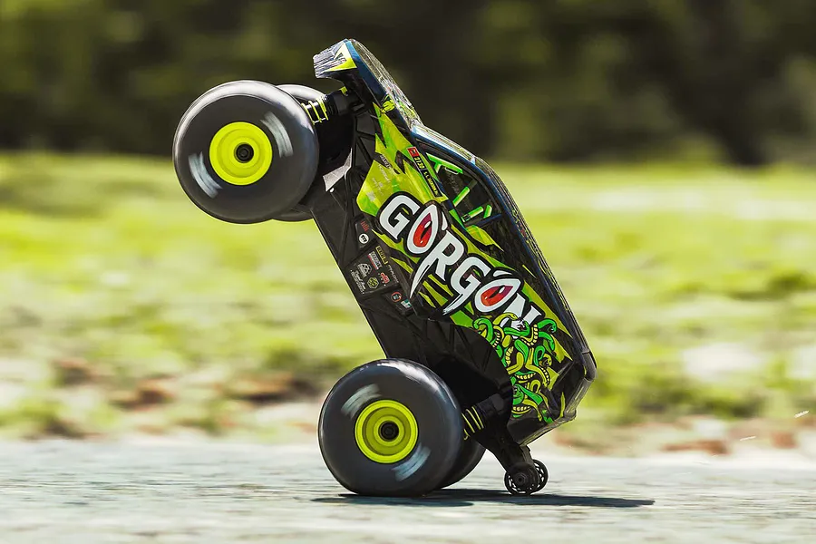 ARRMA Gorgon Grom RC monster truck performing a wheelie outdoors on a paved surface.