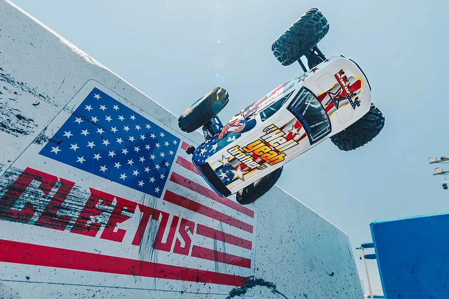 ARRMA Freedom Flyer 223S BLX RC monster truck performing an aerial jump past a painted US flag wall outdoors.