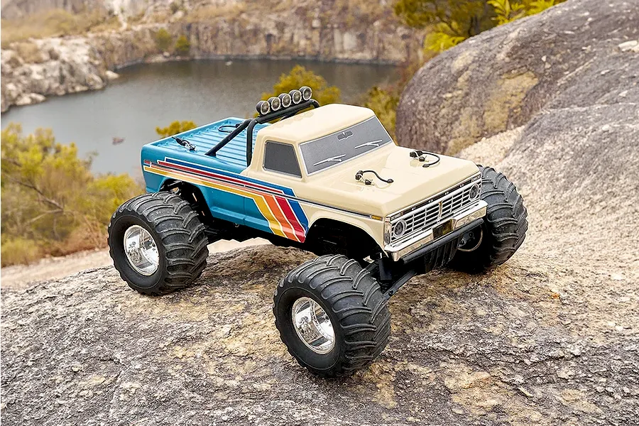 FMS Ford F-100 RS RC monster truck parked on rocky outdoor terrain overlooking water.