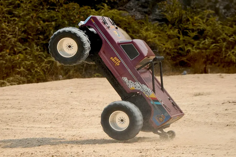 FMS Ford F-100 High Roller RC Monster Truck performing a wheelie on a dirt track outdoors.