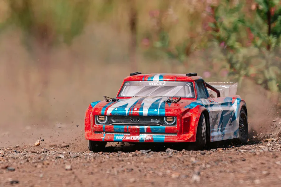 ARRMA Infraction Resto-Mod 4x4 RC truck driving on a dirt track, kicking up dust and gravel in an outdoor setting.
