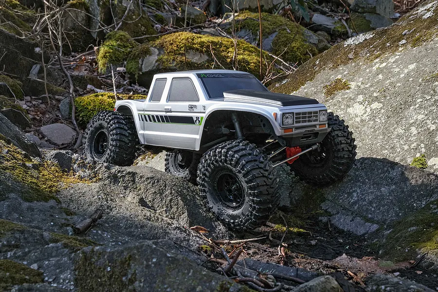 Axial SCX10 III Coyote silver RC rock crawler driving over rough mossy rocks outdoors