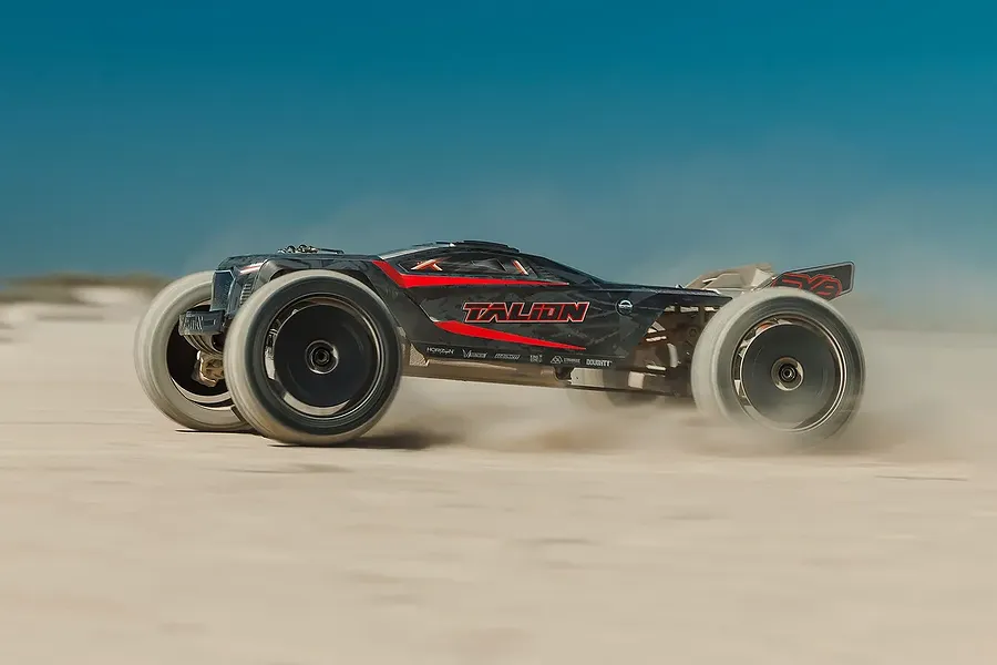 ARRMA Talion 6S BLX RC Truggy driving fast across a sandy outdoor track kicking up dust.