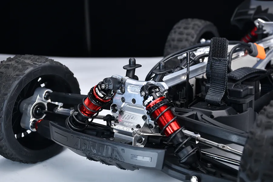 Close-up of a red aluminium front shock tower installed on an RC car chassis with red and black shock absorbers.