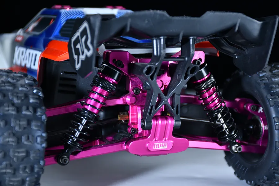 Close-up of an installed purple aluminium rear bumper on an RC car chassis with shock absorbers, a wing mount, and suspension arms.