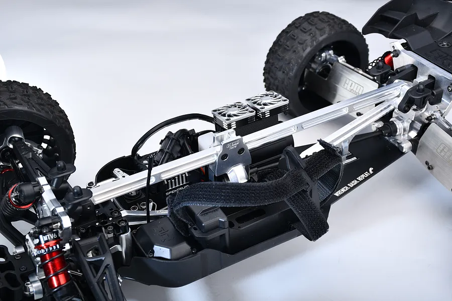 Close-up view of a silver aluminium front and rear chassis brace installed on an RC buggy chassis against a white studio background.