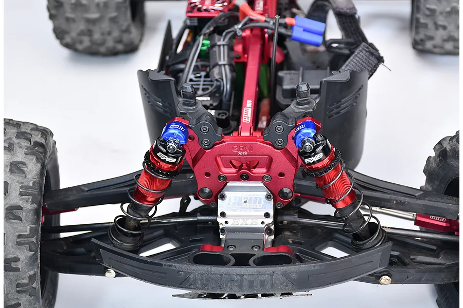Blue aluminium shock cap protectors installed on the front shocks of an RC monster truck, showing the suspension and chassis setup.