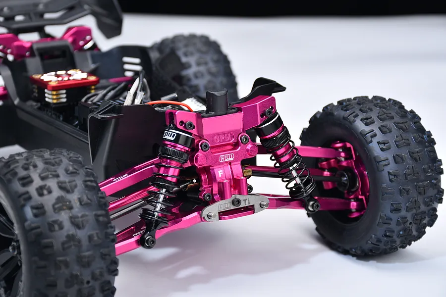 Close-up of pink aluminium front suspension upgrades and shock tower installed on an RC car chassis.