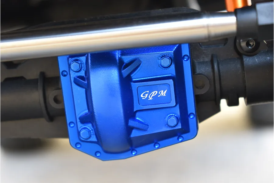 Blue anodized aluminium GPM gearbox cover installed on an RC vehicle axle housing with a silver link bar.