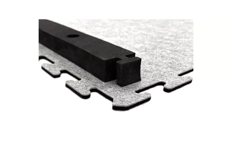 Close-up of interlocking grey carpet track tile with a black track barrier attached.