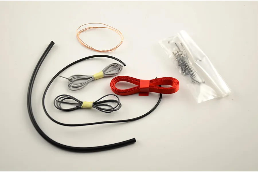Model kit parts including various wires, tubing, coiled springs, and hardware in a plastic bag on a white background.