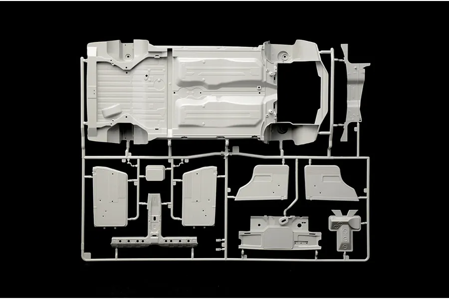 A light grey plastic model kit runner containing a car chassis floorpan and interior panel parts against a black background.