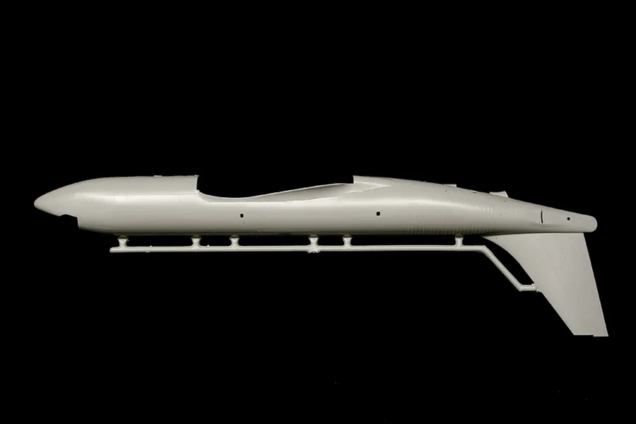 Unpainted light grey plastic model kit fuselage part attached to a sprue against a black background.