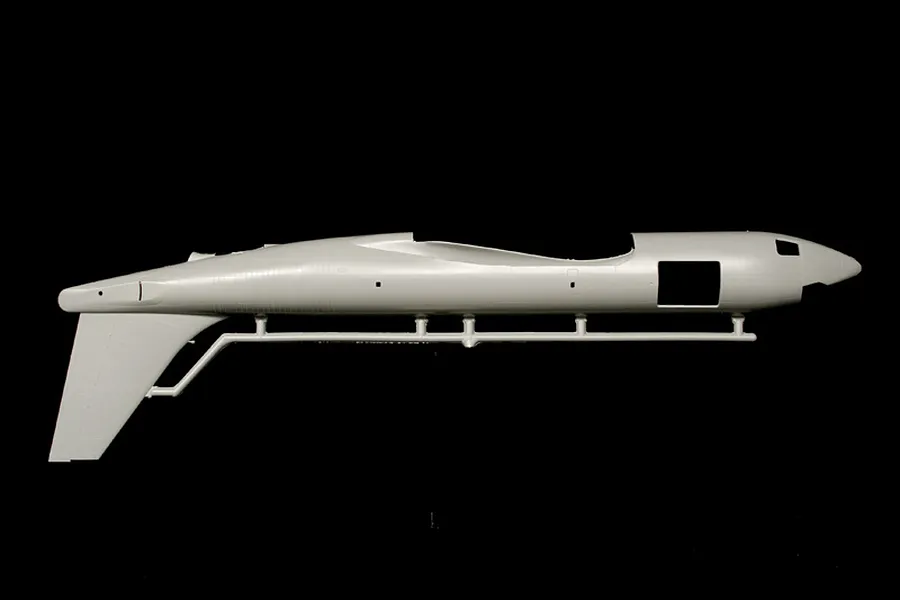 Molded plastic model airplane fuselage attached to a parts sprue against a dark background.
