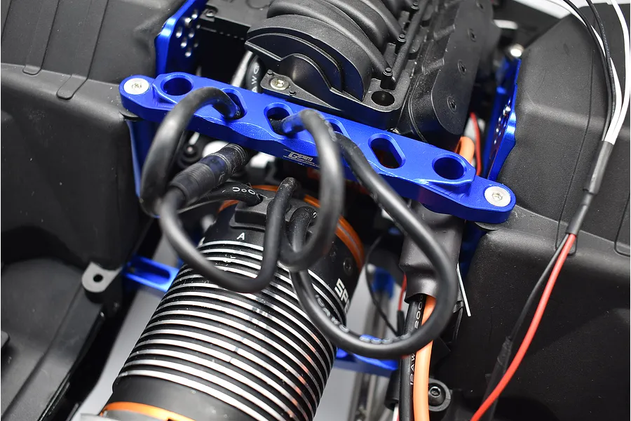 GPM blue aluminium front chassis brace installed on an RC vehicle chassis with black motor and wires.