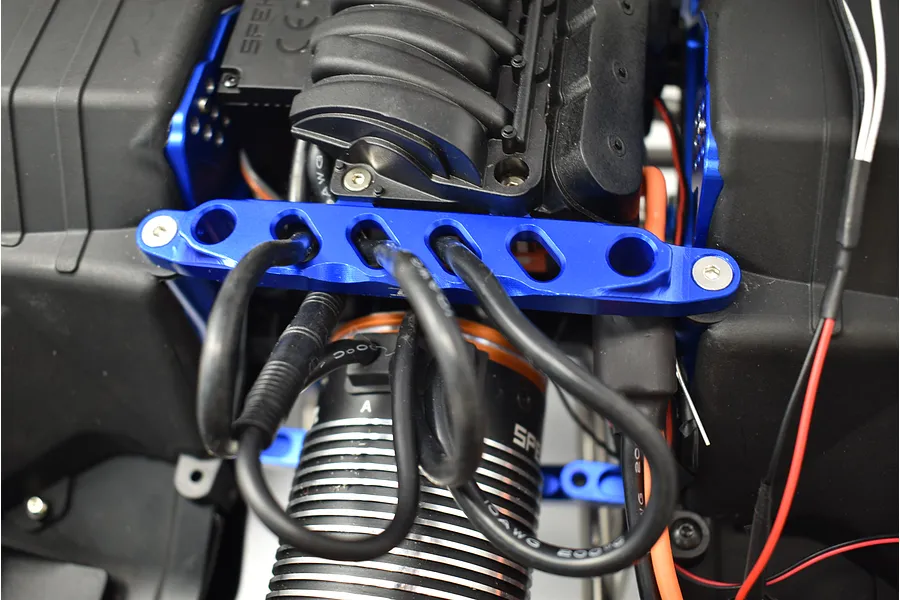 Close-up view of a blue anodized aluminium front chassis brace installed on an RC car, with wires running over it.