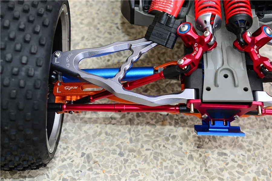 Close-up of installed red aluminium turnbuckles and suspension upgrades on an RC model car chassis.
