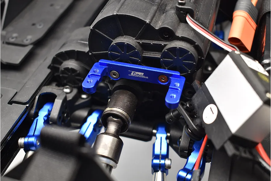 Close-up of a blue aluminium transmission servo mount installed on an RC car chassis near the transmission and servo.