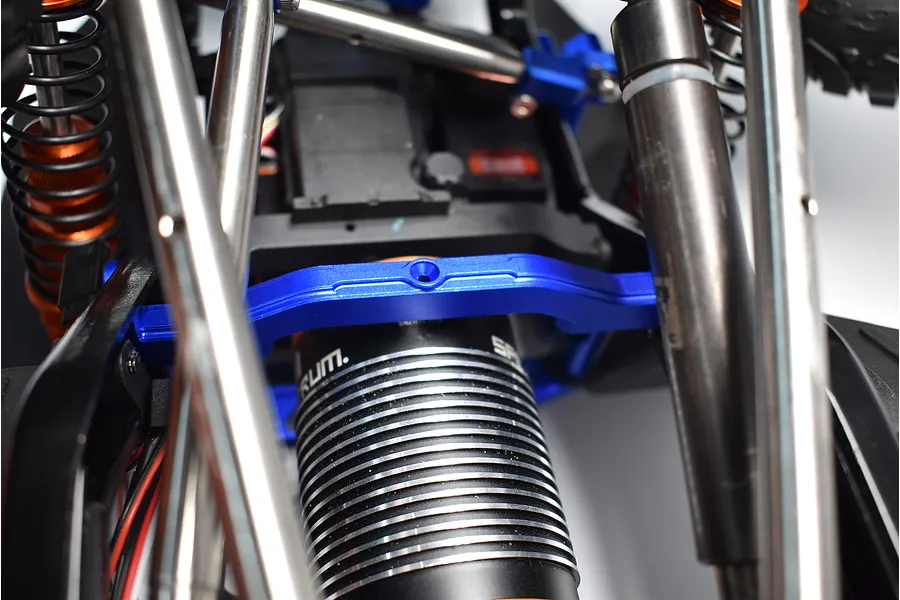 Close-up of a blue aluminium chassis brace installed on an RC crawler chassis near the motor and suspension.