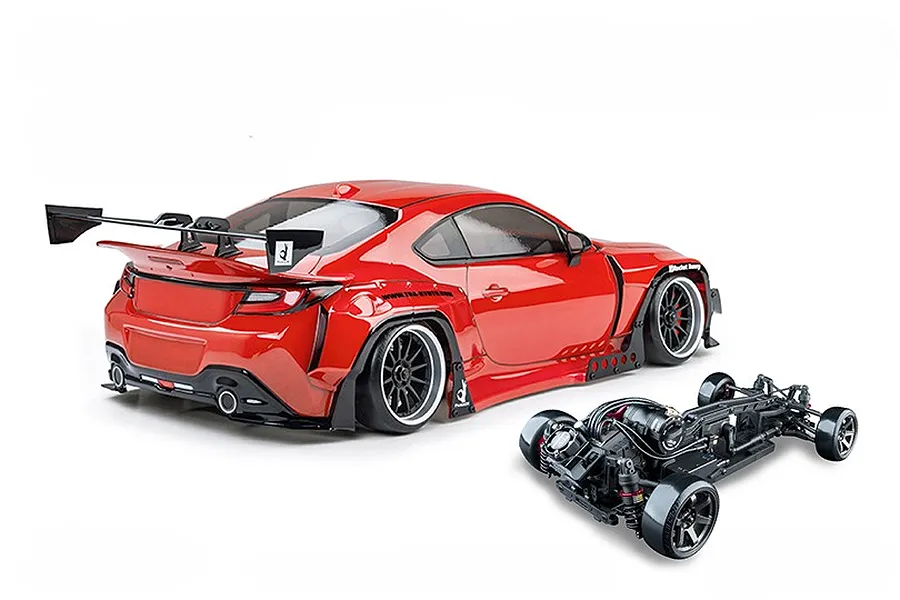 Rear-three-quarter view of an assembled red radio control drift car with a large rear wing and a separate black RC chassis shown in the foreground.
