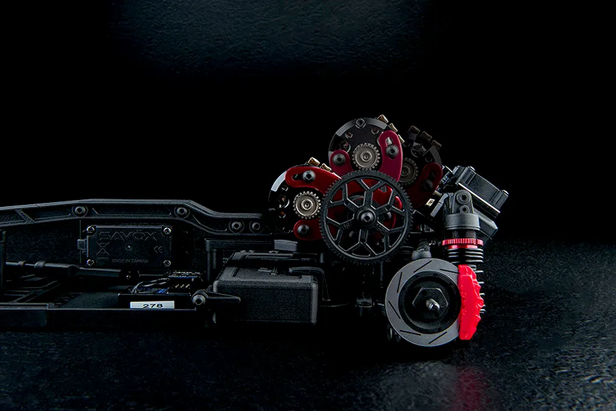 Close-up side profile of an RC car chassis showcasing the internal gears, suspension, and electronics against a dark background.