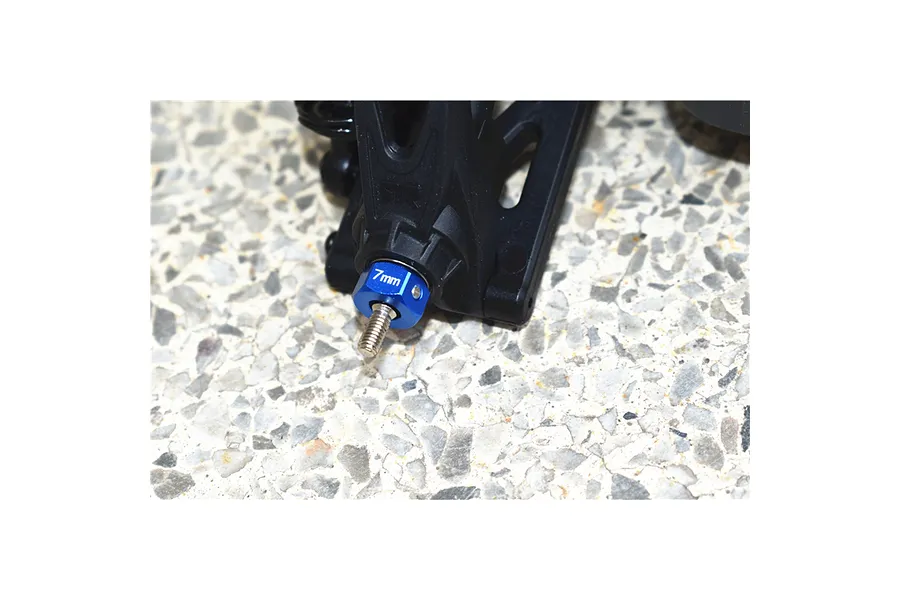 Blue anodised aluminium wheel hex adaptor installed on an RC car suspension arm over a concrete background.