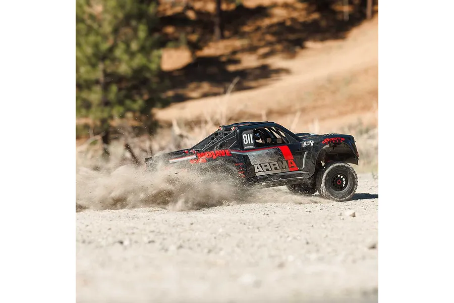 ARRMA MOJAVE 6S RC desert truck driving fast on a dirt track, kicking up a large cloud of dust in an outdoor setting.