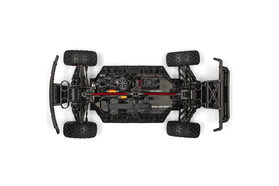 Top-down studio view of the RC short course truck chassis showing electronics layout, battery strap, and shock absorbers.