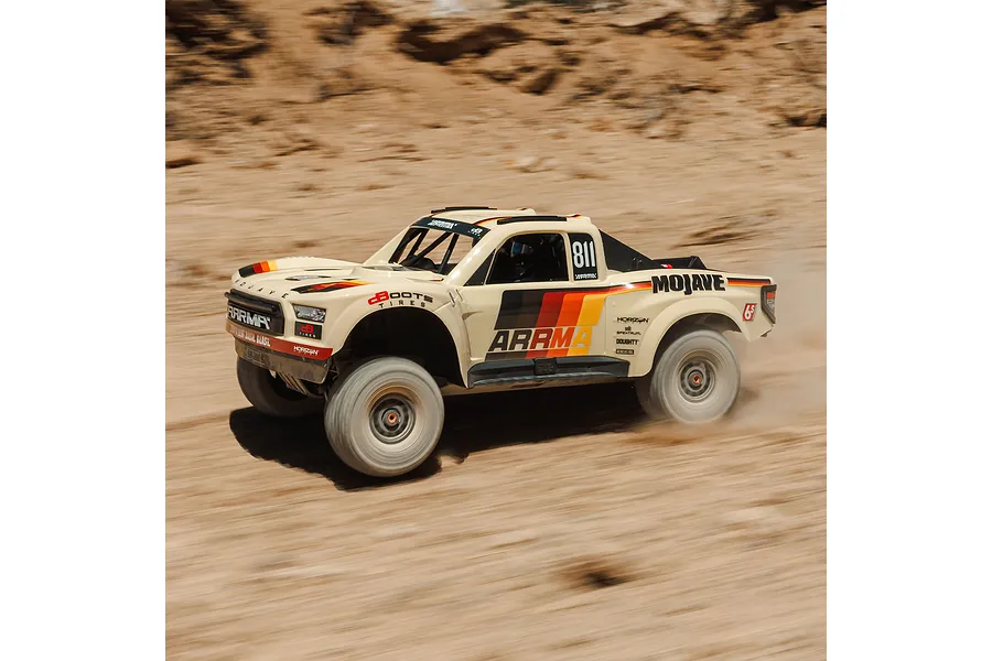 ARRMA Mojave 6S beige RC short course truck driving fast through a dusty desert landscape kicking up sand.