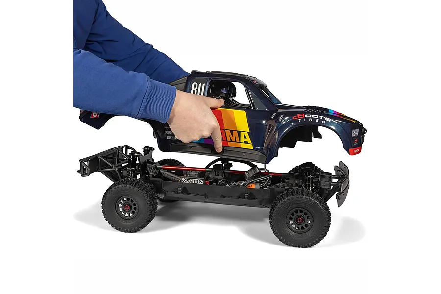 Person lifting the blue and multicolored body shell off the chassis of an ARRMA Mojave 6S RC short course truck.