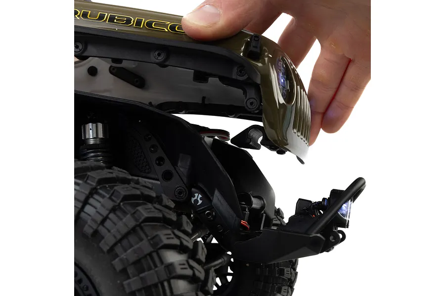 Close-up of a person's hand lifting the green plastic body hood of an Axial RC rock crawler to show internal chassis components.