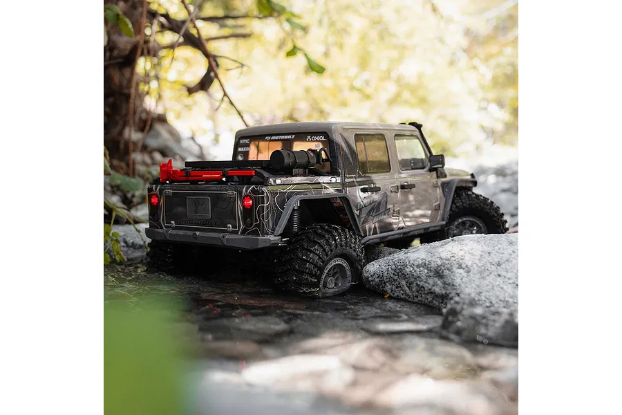 Axial SCX10 III Motobilt Valyrian Jeep JT Gladiator RC rock crawler driving through a shallow stream surrounded by rocks and foliage.