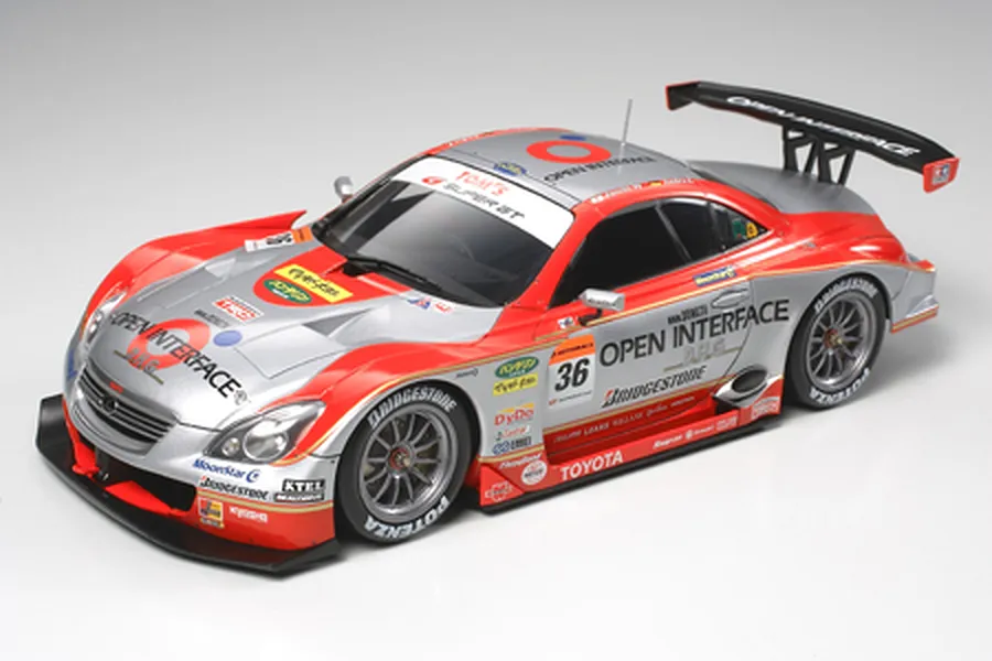A high-angle studio shot of a completed 1/24 scale Tamiya Lexus SC430 2006 Tom's Open Interface race car model, featuring red and silver livery.