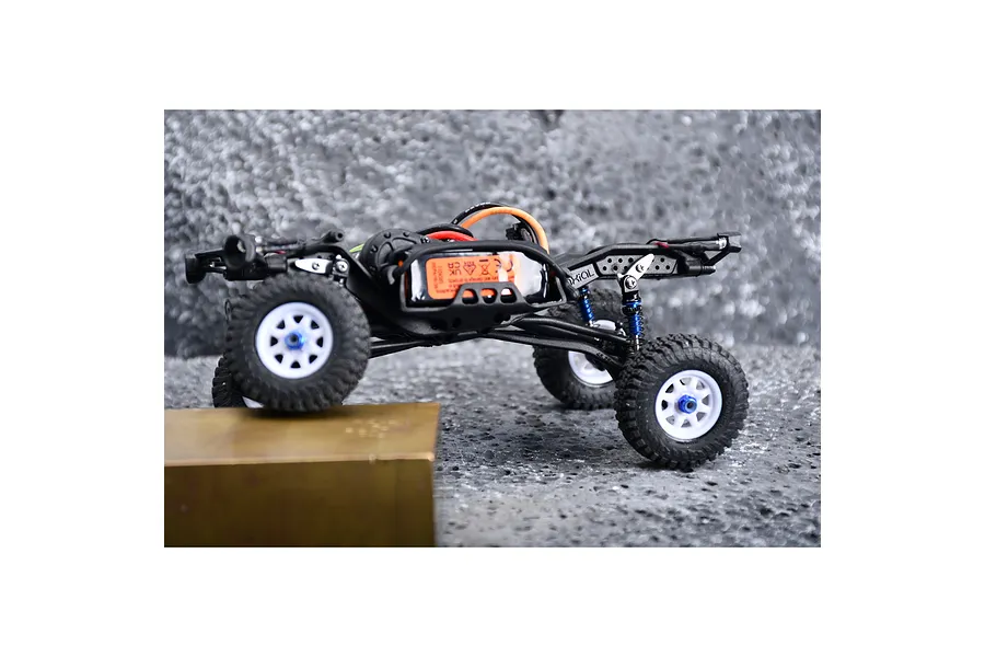 Side profile of an RC crawler chassis with blue flex blade extensions installed on the suspension.