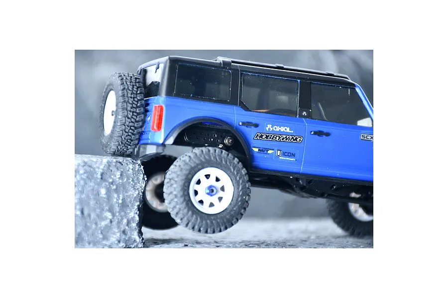 Blue RC crawler car on rocky terrain showcasing suspension articulation and flex blade extensions.