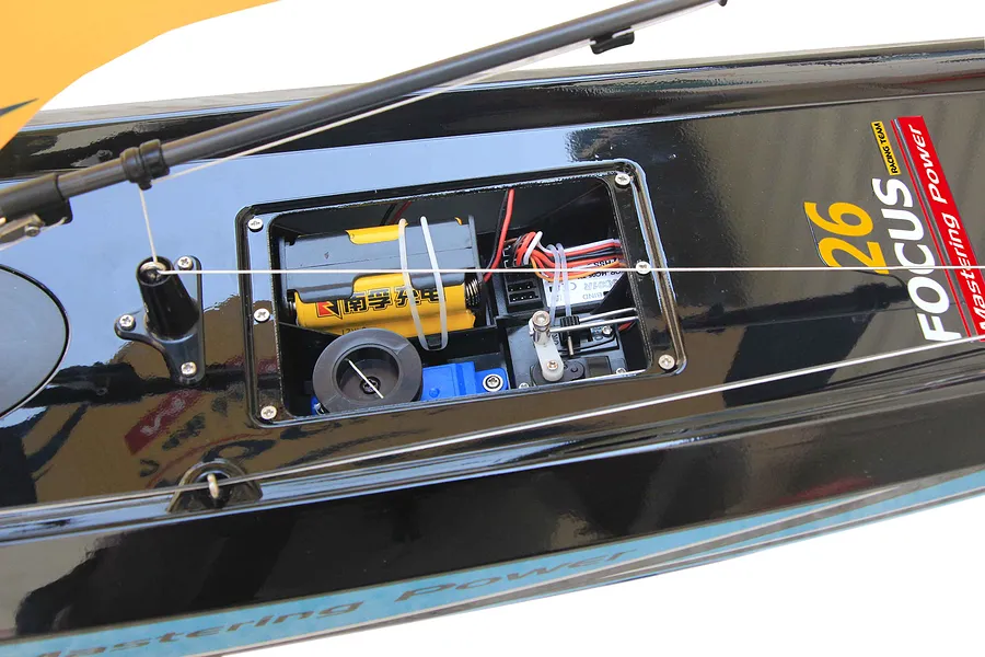 Close-up of the open electronic hatch on the deck of a black Joysway Focus V3 RC sailboat showing internal electronics and battery pack.