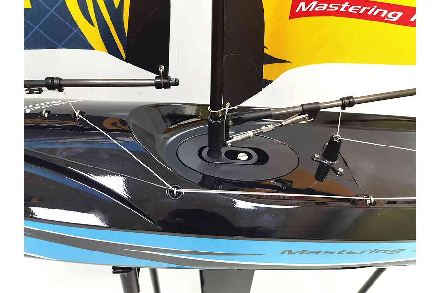 Close-up of the deck and mast rigging on a Joysway Focus V3 RC sailboat with a glossy black hull and blue stripe.