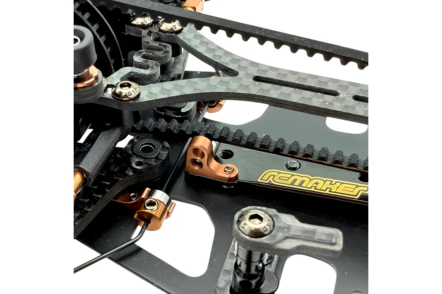 Close-up view of an RC Maker rear belt tensioner and carbon fiber chassis components on an RC car.