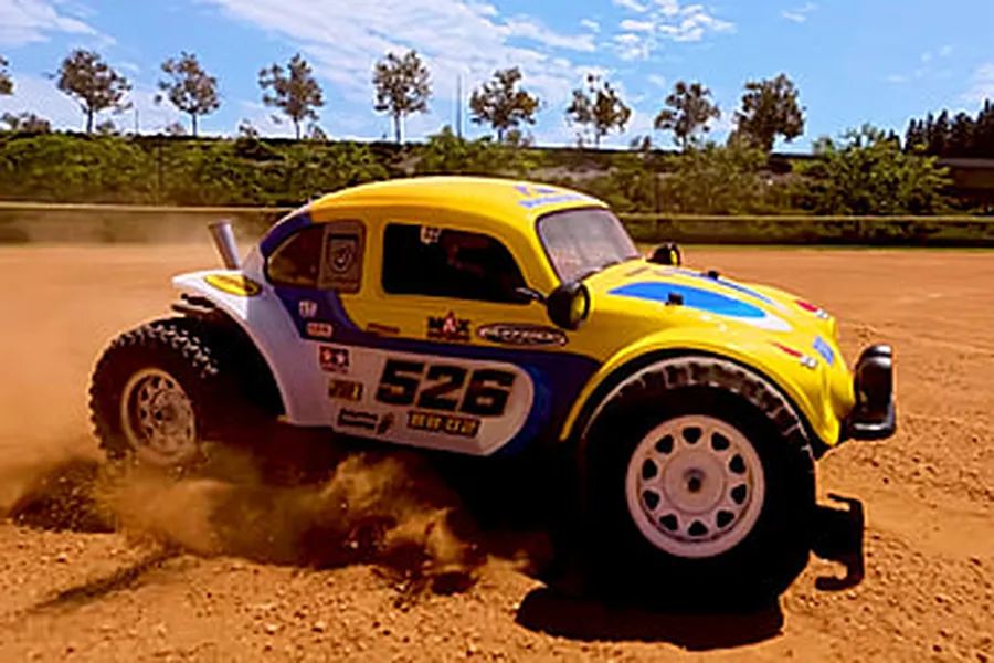 Yellow and blue Volkswagen RC buggy kicking up dust on a dirt track outdoors.