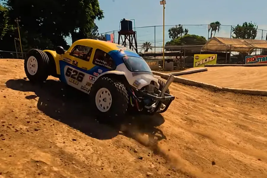 Tamiya Volkswagen Dune Beetle RC buggy driving on an outdoor dirt track, kicking up dust.
