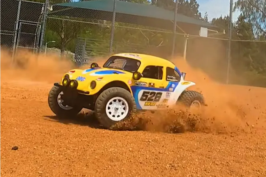 Tamiya BB-02 Volkswagen Dune Beetle RC buggy driving on a dirt track, kicking up dust and dirt.