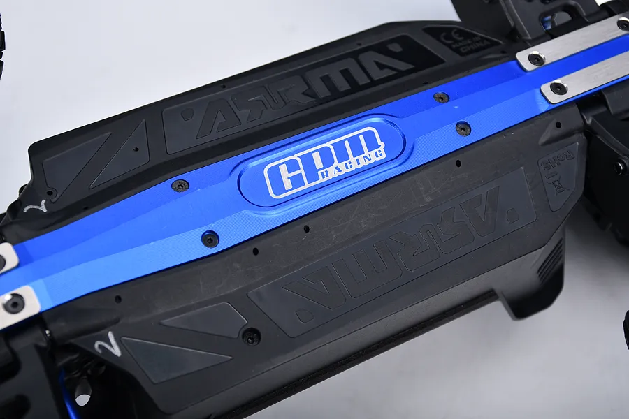 Close-up of a blue anodized GPM Racing aluminium chassis brace and skid plate installed on an RC car chassis.