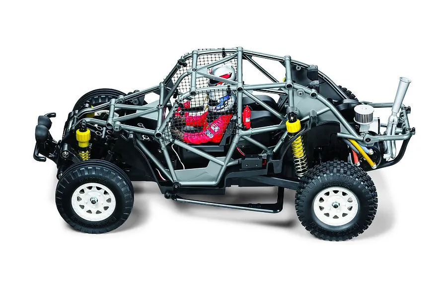 High angle side profile of the Tamiya BB-02 Volkswagen Dune Beetle RC buggy showing its roll cage, driver figures, and white wheels against a white background.